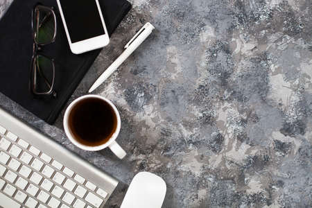 Modern gray work office desk table with laptop, keyboard, smartphone and other business accessories, supplies with cup of coffee. Top view, flat lay.の写真素材