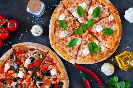 Hot testy pizza with tomatoes, mozzarella, mushrooms, olives, red pepper and basil on black concrete background. Copyspace. Top view. Banner.の写真素材