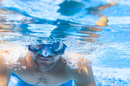 Young man in diving mask swimming the front crawl in a pool, taken under water, summer party