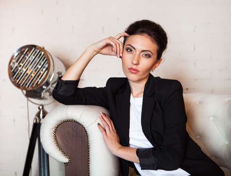 Portrait of a young woman with a beautiful smile sitting on sofa in minimalistic inteior. Fashion and beautyの写真素材