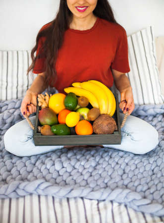 Young girl wearing pastel colored home clothes with tray full of fresh fruit. Summer healthy raw vegan clean eating breakfast in bed concept. Top view, copy space.の写真素材