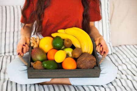Young girl wearing pastel colored home clothes with tray full of fresh fruit. Summer healthy raw vegan clean eating breakfast in bed concept. Top view, copy space.の写真素材