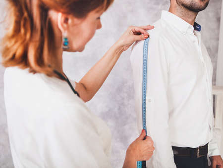 Woman tailor takes measures with male models. Mid section portrait of tailor fitting bespoke suit to modelの写真素材