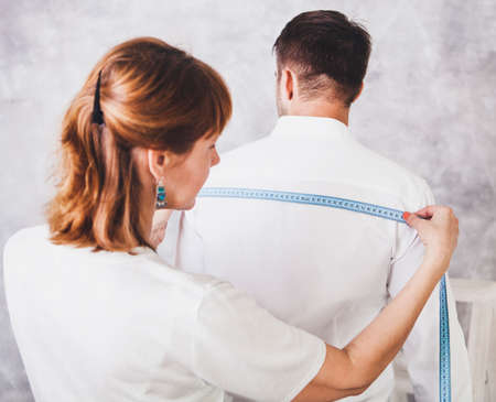 Woman tailor takes measures with male models. Mid section portrait of tailor fitting bespoke suit to modelの写真素材