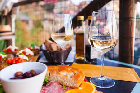 Romantic dinner for two at sunset. White wine and Tasty italian snack: fresh bruschettes  and meat on the board in outdoor cafe with amazing view in Manarola, Italyの写真素材