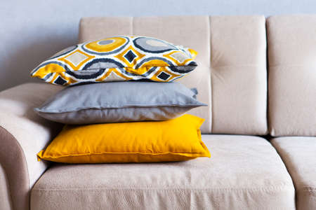 Multi-colored pillows on a beige fabric sofa, the concept of home comfort and cozy, copy space,...