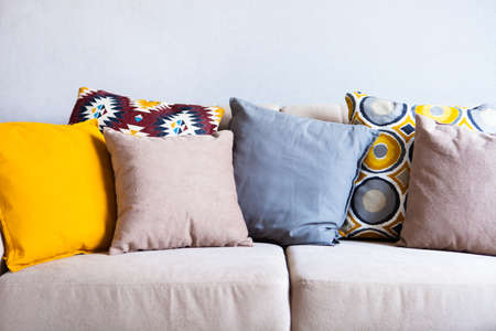 Multi-colored pillows on a beige fabric sofa, the concept of home comfort and cozy, copy space,...