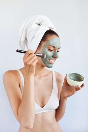 Young beautiful woman in face mask of therapeutic blue mud. Spa treatment, self care and healthy skin. Copy space, white backgroundの写真素材
