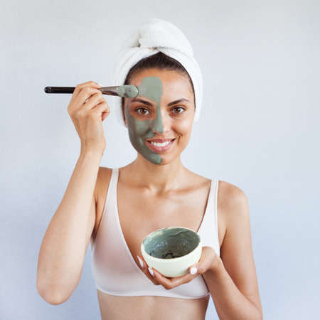 Young beautiful woman in face mask of therapeutic blue mud. Spa treatment, self care and healthy skin. Copy space, white backgroundの写真素材