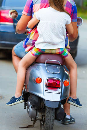 Father and daughter riding a vintage scooter in the street wearing hats. Holiday and travel family conceptの写真素材