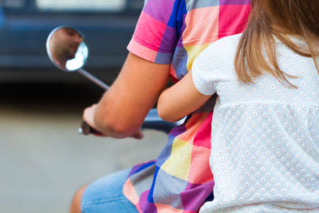 Father and daughter riding a vintage scooter in the street wearing hats. Holiday and travel family...