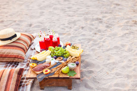 Picnic on the beach at sunset in the style of boho. Concept outdoors evening healthy meal with fruit and juice.の写真素材