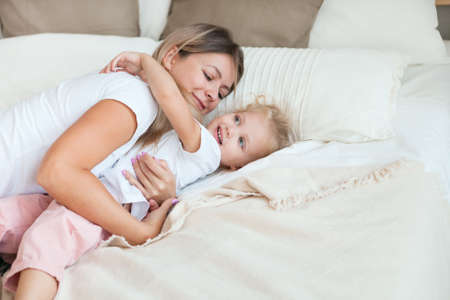 Mother and her daughter child girl playing and hugging in bedroom. Happy loving family.の写真素材