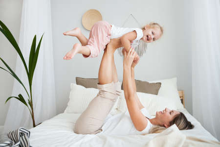 Mother and her daughter child girl playing and hugging in bedroom. Happy loving family.