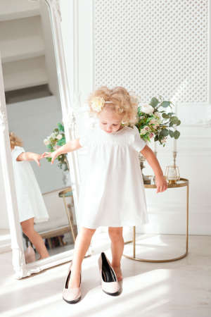Little pretty girl in white dress trying on mummy's shoes, indoorの写真素材