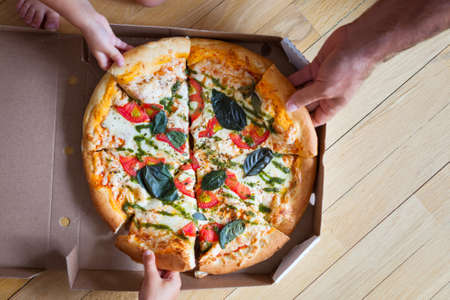 Family group dinner. Hands taking slices of pizza with box. Friends Happiness Enjoying Dinning...