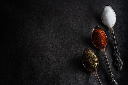 Spices pepper salt dried herbs in a teaspoon close-up on a black background flat layの写真素材