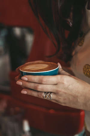 a cup of coffee in the hands of a girl cappuccino latの写真素材