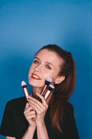 girl makeup artist with makeup brushes on a blue background. the brunette is thin.