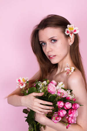 skinny girl holding flowers on a pink background. brunetteの写真素材