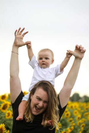 brunette woman young mom with cute baby blonde son on a field of sunflowers.の写真素材