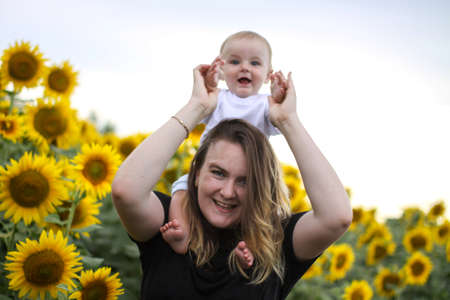 brunette woman young mom with cute baby blonde son on a field of sunflowers.