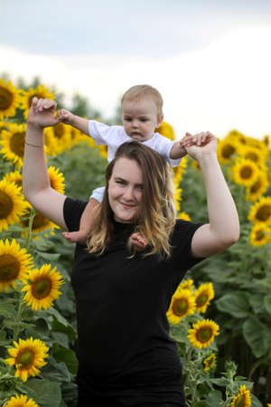 brunette woman young mom with cute baby blonde son on a field of sunflowers.の写真素材