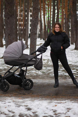 young mother on a walk with her baby. girl with a baby in a stroller in the winter on a walk.