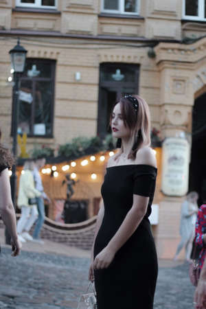 girl in a black short dress on the evening street. against the backdrop of lights, shops.の写真素材