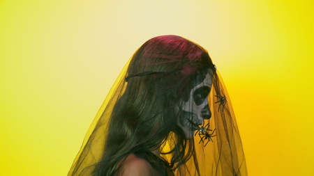 Halloween, girl with make-up skeleton on half face, dressed as witch, posing on bright yellow background. close-upの写真素材