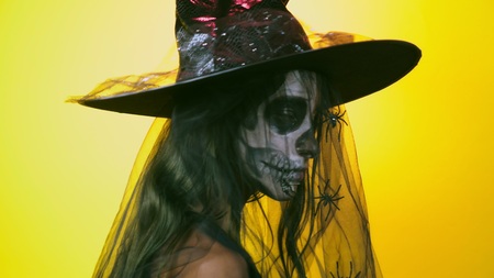 Halloween, girl with make-up skeleton on half face, dressed as witch, posing on bright yellow...