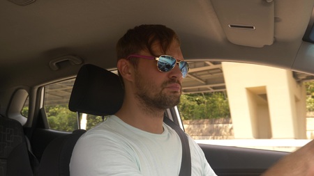 a young handsome man in sunglasses leads a car at high speed, along a highway with a view of the...