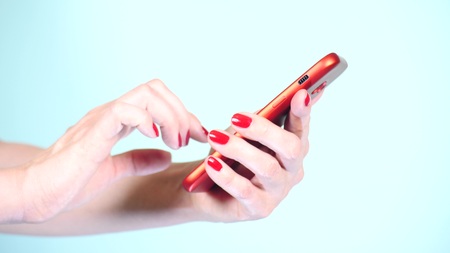 close-up, female hands with red manicure use a smartphone on a colored backgroundの写真素材