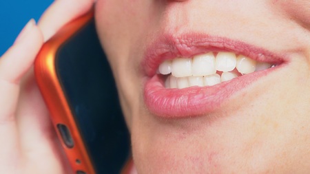 close-up, female lips without makeup talking on a red mobile phone, against a blue backgroundの写真素材