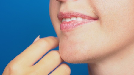 close-up, women's lips without make-up, the girl touches her face with her hand. on a blue background.の写真素材