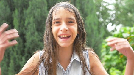 Close-up. portrait of a young girl looking at the rain in nature with wet hair. the girl rejoices in the pouring rain, drops of water fall on her faceの写真素材