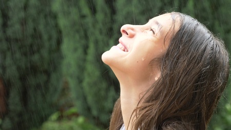 Close-up. portrait of a young girl looking at the rain in nature with wet hair. the girl rejoices in the pouring rain, drops of water fall on her faceの写真素材