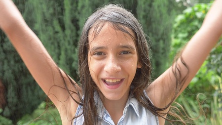 Close-up. portrait of a young girl looking at the rain in nature with wet hair. the girl rejoices in the pouring rain, drops of water fall on her face.の写真素材