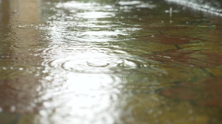 drops of pouring rain fall into puddles on the sidewalk. close-up.の写真素材