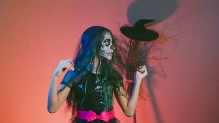 Halloween, girl with makeup skeleton on half face, dressed as a witch, posing and dancing on a red background.の写真素材