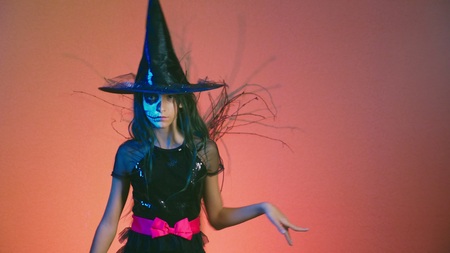 Halloween, girl with makeup skeleton on half face, dressed as a witch, posing and dancing on a red background.の写真素材