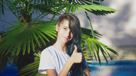 beautiful brunette girl posing against a background of palm leaves. A girl teenager with blue long curly hair. summer sunny day.の写真素材