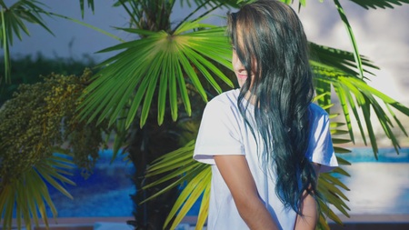 beautiful brunette girl posing against a background of palm leaves. A girl teenager with blue long curly hair. summer sunny day.の写真素材