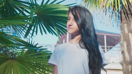 beautiful brunette girl posing against a background of palm leaves. A girl teenager with blue long curly hair. summer sunny day.の写真素材