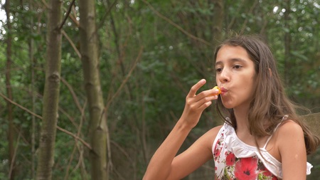 Cute little girl brunette, eating fruit and talking. Nature background.の写真素材