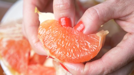 Female hands cleanse the grapefruit. close-up, female hands with red nail polish.の写真素材