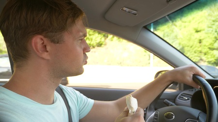 the man at the wheel of the car, eats fast food, while the car is moving. in a summer sunny day.の写真素材
