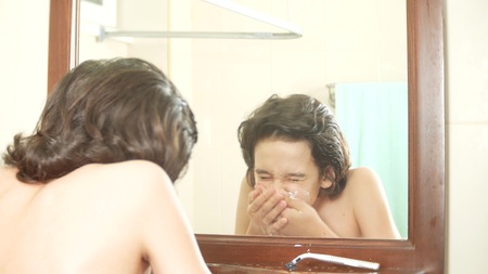 boy teenager is washing his face in front of a mirror.の写真素材
