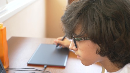 handsome modern boy teenager working on a graphic tablet. he looks at the laptop screen.の写真素材