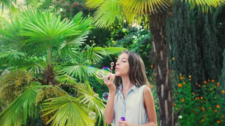 girl teen brunette blowing soap bubbles against a tropical park background.の写真素材